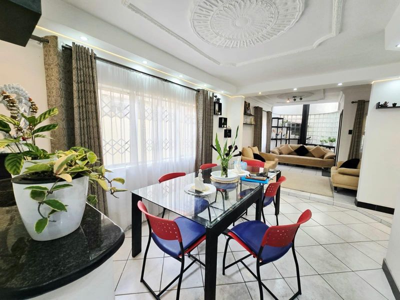 Open plan living and dining area featuring decorative ceiling roses, tiled flooring, and large windows with security bars.