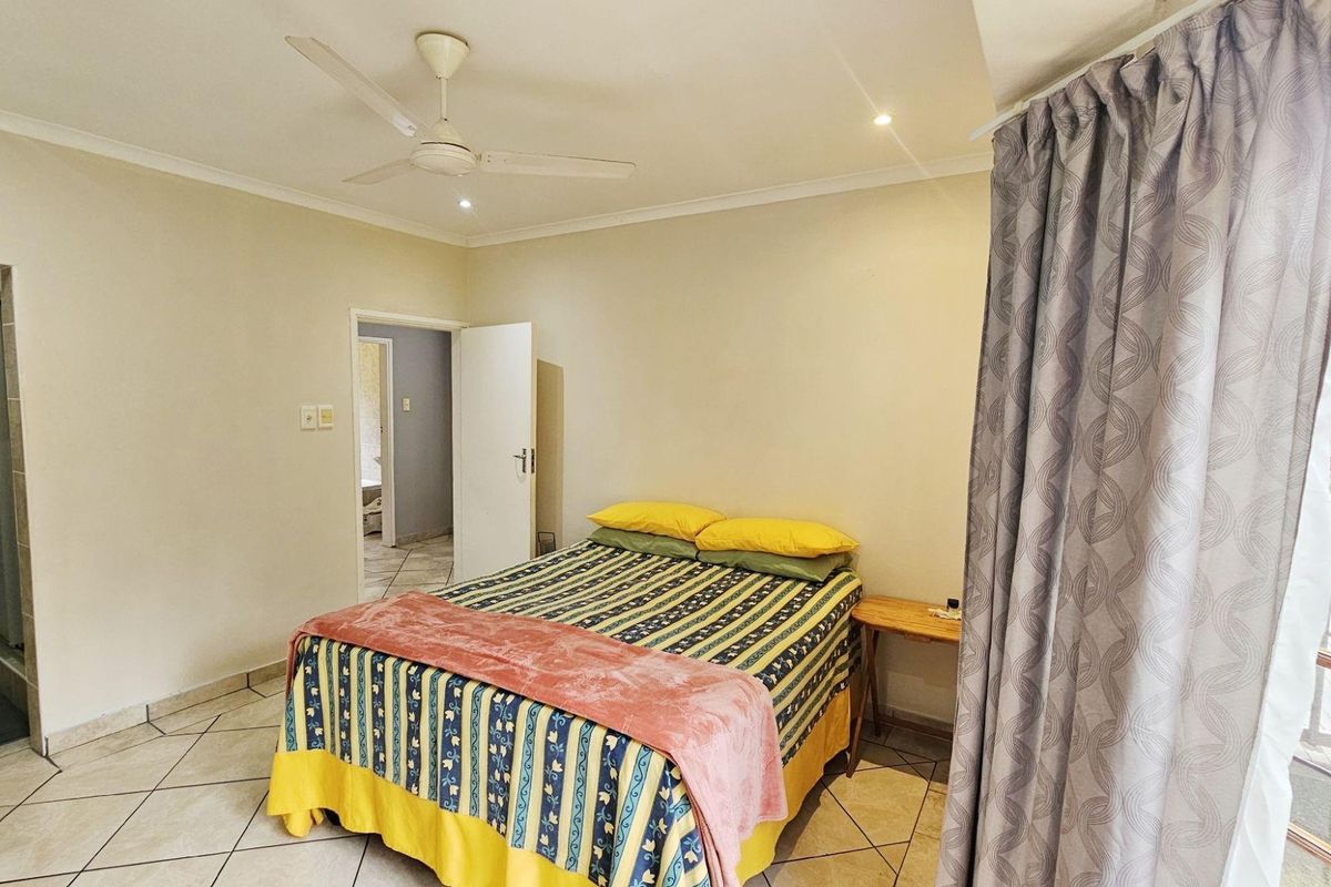 A bedroom featuring tiled flooring, a ceiling fan, and an en-suite bathroom, with direct access to an outdoor balcony area.