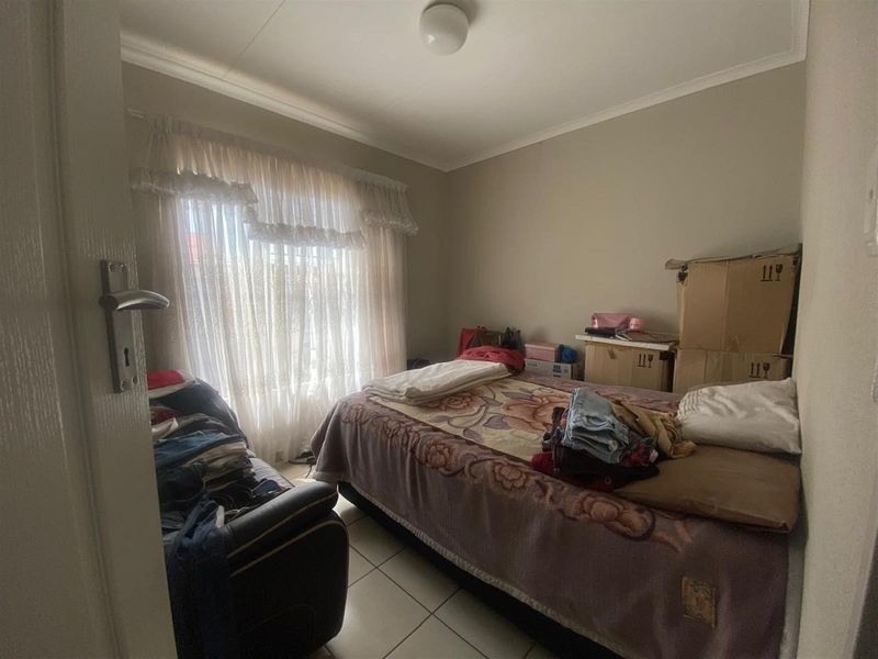 A standard bedroom featuring tiled flooring and a window with fitted curtain rails.