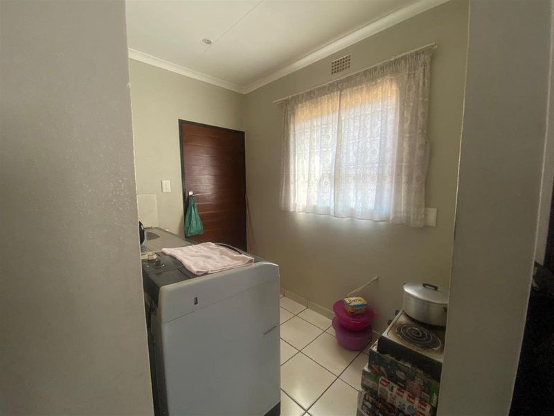 A functional laundry area featuring tiled flooring, a window with curtaining, and a dedicated space for laundry appliances.
