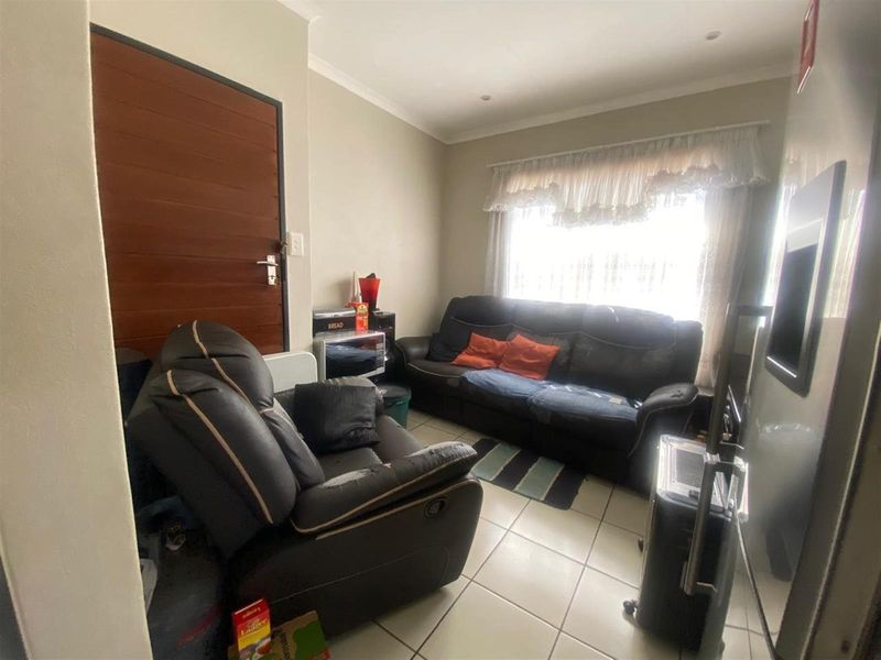 A compact living room featuring tiled flooring, a solid timber entrance door, and a large window with natural light.