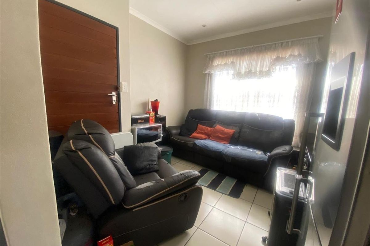 A compact living room featuring tiled flooring, a solid timber entrance door, and a large window with natural light.