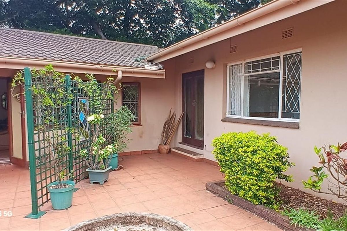 A paved rear patio area featuring a covered entrance, tiled flooring, and established garden beds, providing a functional outdoor living space.