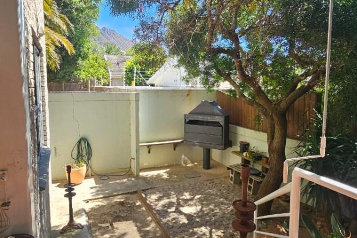 A rear outdoor area featuring a built-in braai, paved patio space, and established trees, offering a private setting for outdoor entertaining.