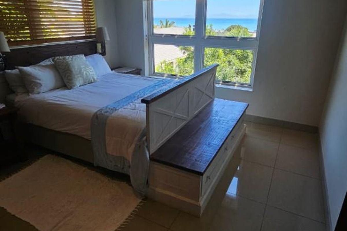 A bedroom featuring large windows with ocean views, tiled flooring, and wooden blinds, offering a bright and airy atmosphere.