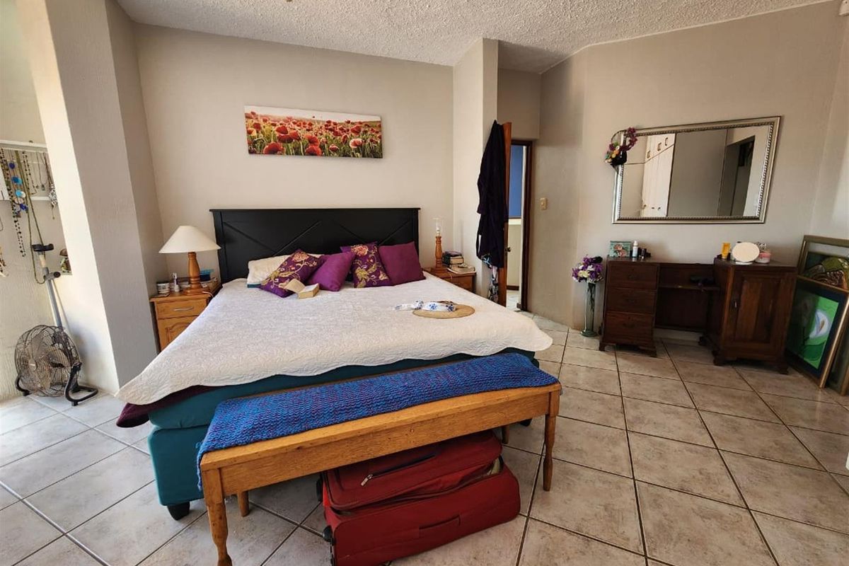 A spacious bedroom featuring neutral walls, tiled flooring, and a doorway leading to an adjoining room.