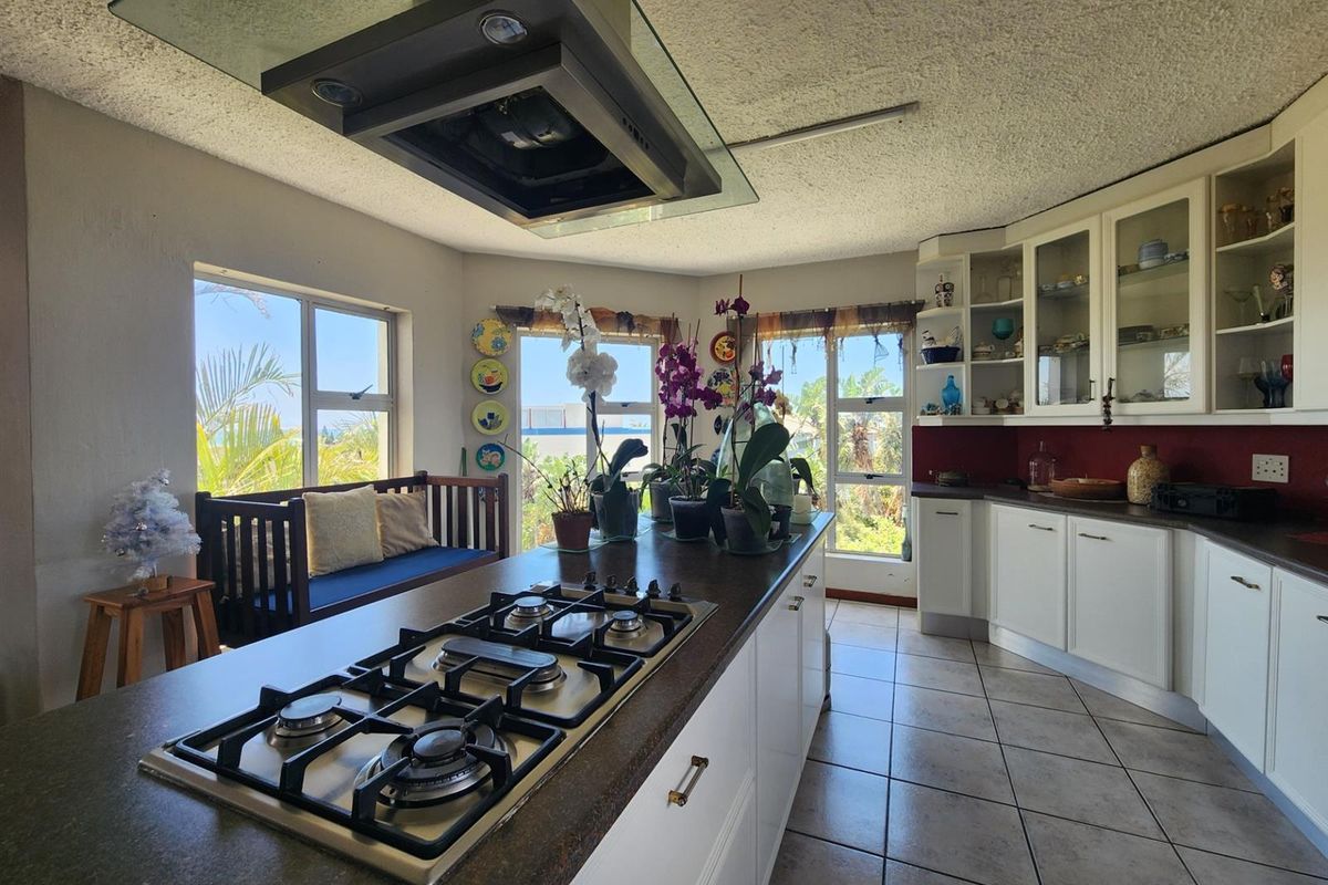 Spacious kitchen featuring a central island with a built-in gas hob, overhead extractor fan, ample cabinetry, and large windows providing natural light.