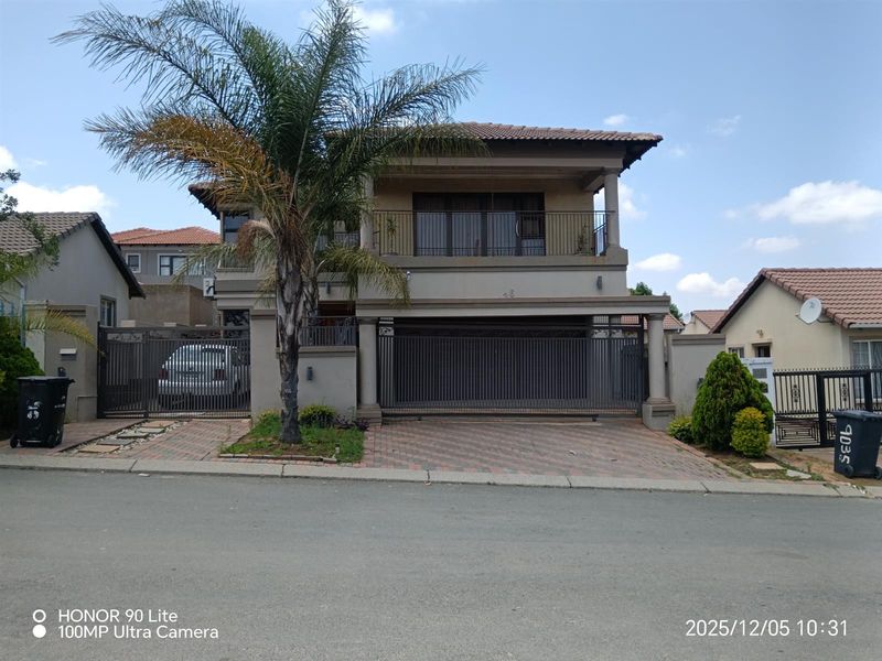 Front elevation of a double-story residential property featuring a paved driveway, secure metal gate, and an upper-level balcony.
