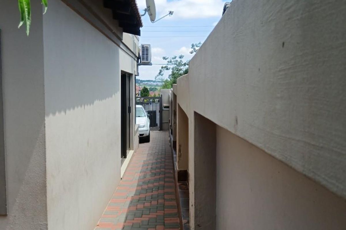 A narrow paved side walkway between the house exterior and the boundary wall, featuring an external air conditioning unit and satellite dish.
