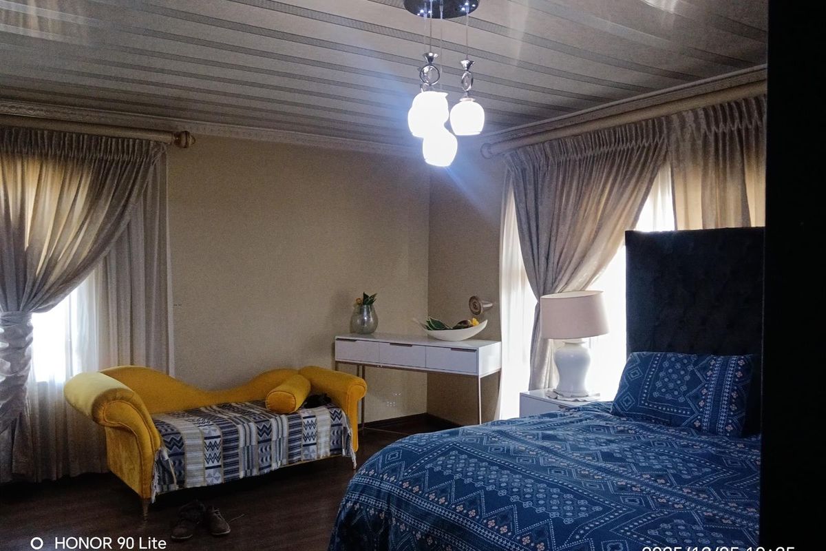A bedroom featuring laminate flooring, ceiling panels, and a central pendant light fixture, with large windows dressed in curtains.