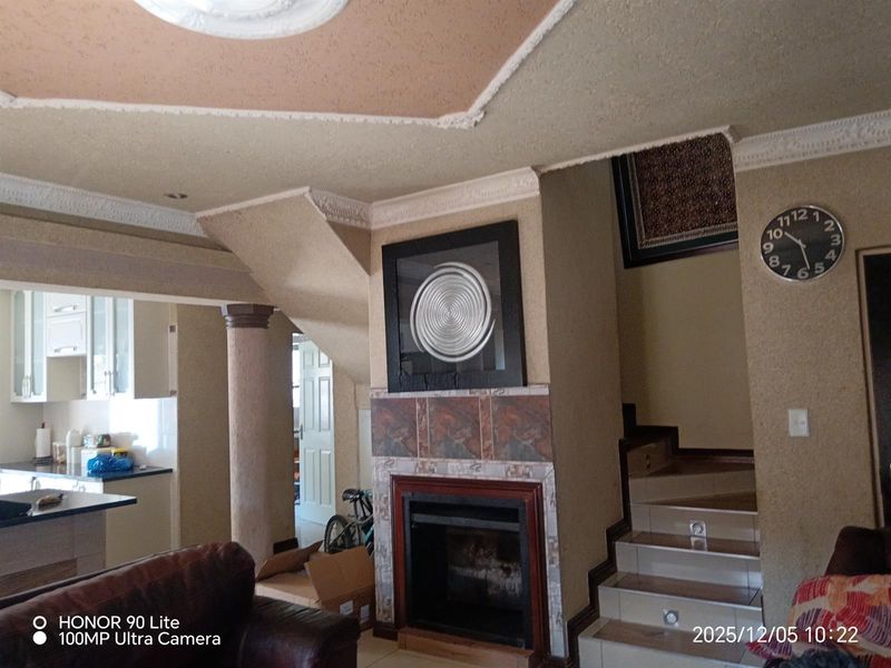 Open plan living area featuring a tiled fireplace, decorative ceiling cornices, and a staircase leading to the upper level, adjacent to the kitchen.