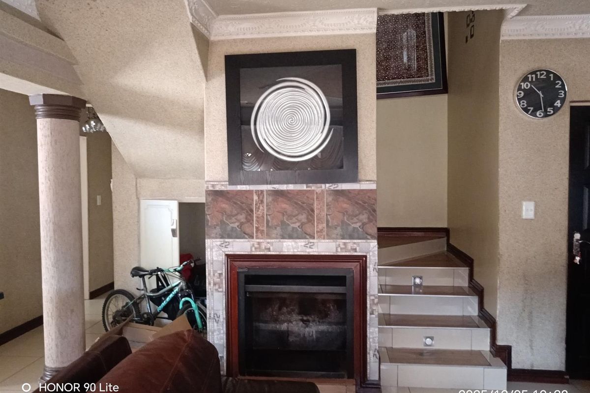 Living room featuring a central fireplace with tiled surround, a staircase, and decorative architectural columns.