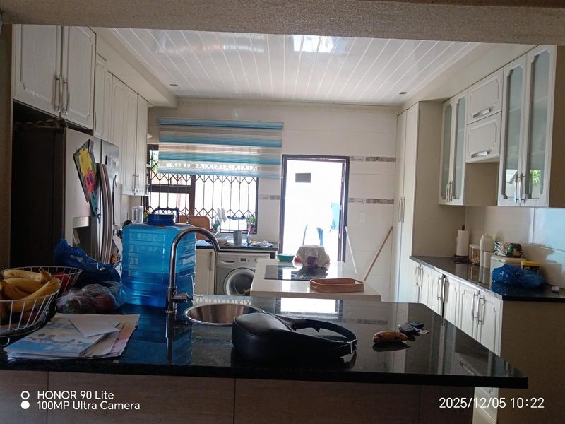 A functional kitchen featuring granite countertops, ample built-in cabinetry, and an integrated washing machine, with direct access to the exterior.