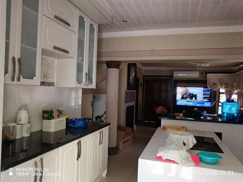 Open-plan kitchen and living area featuring white cabinetry, black granite countertops, a central island, and tiled flooring with a decorative column.