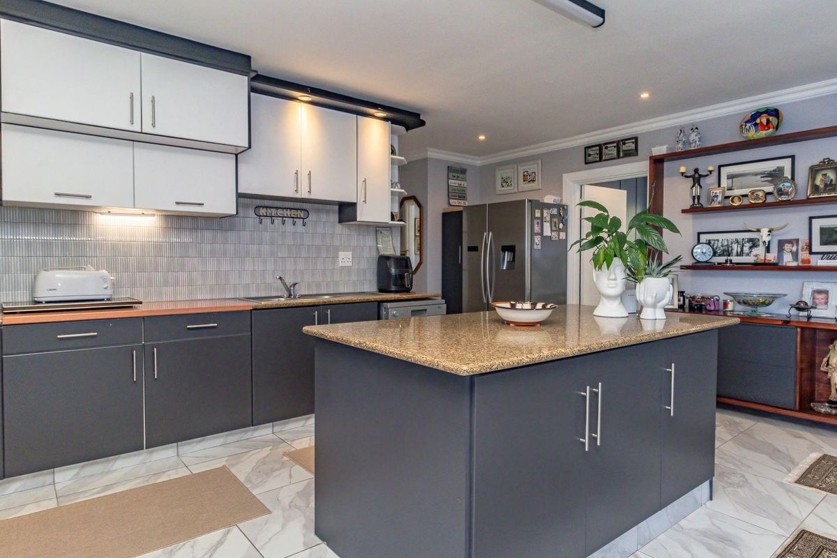Modern kitchen featuring a central island with granite countertop, two-tone cabinetry, tiled backsplash, and integrated shelving.