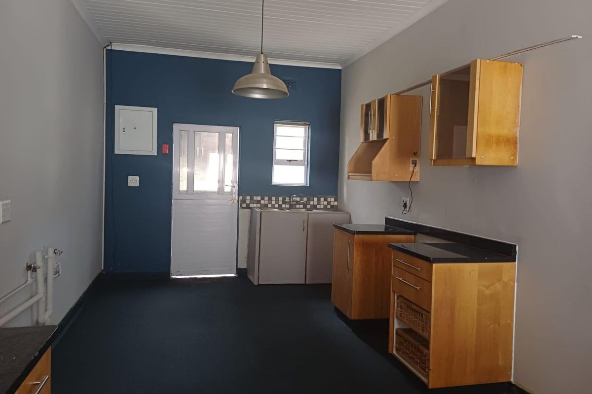 A functional kitchen area featuring wooden cabinetry, dark countertops, a single sink, and a stable-style exterior door with direct access.