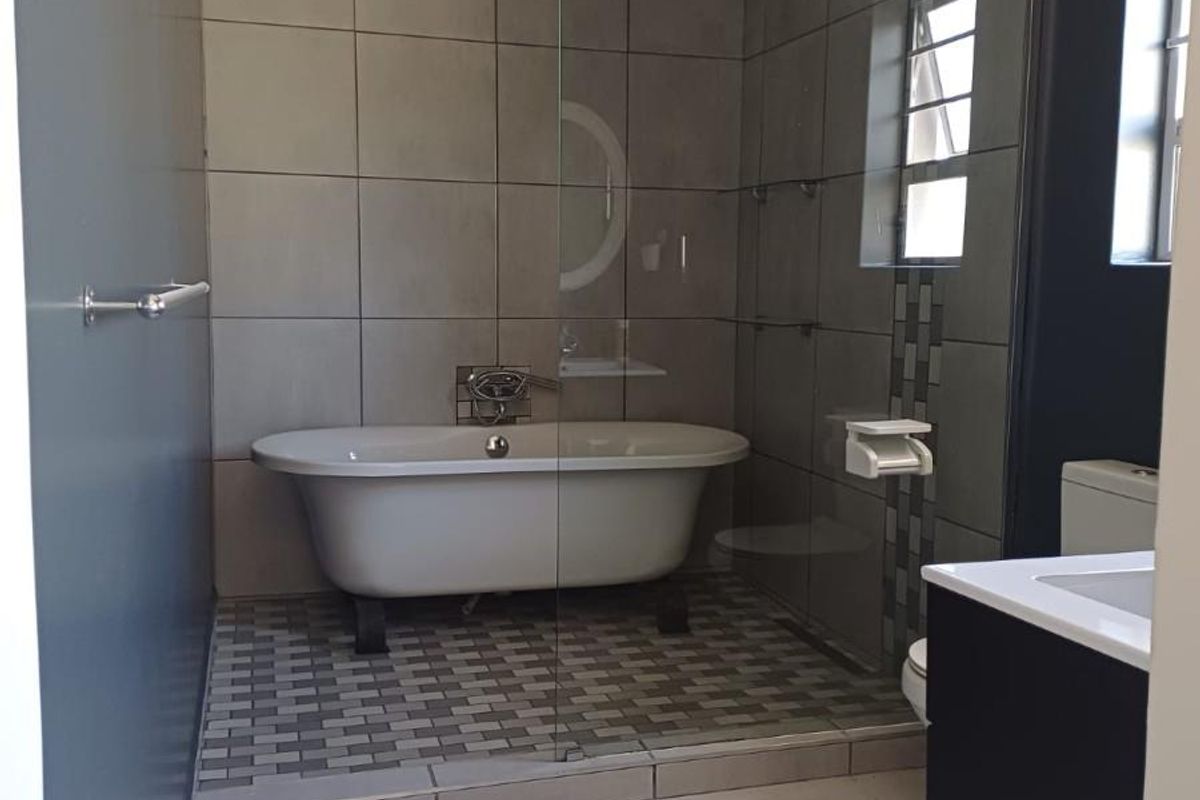 Modern bathroom featuring a freestanding bathtub, glass-enclosed shower, tiled flooring, and a vanity unit.
