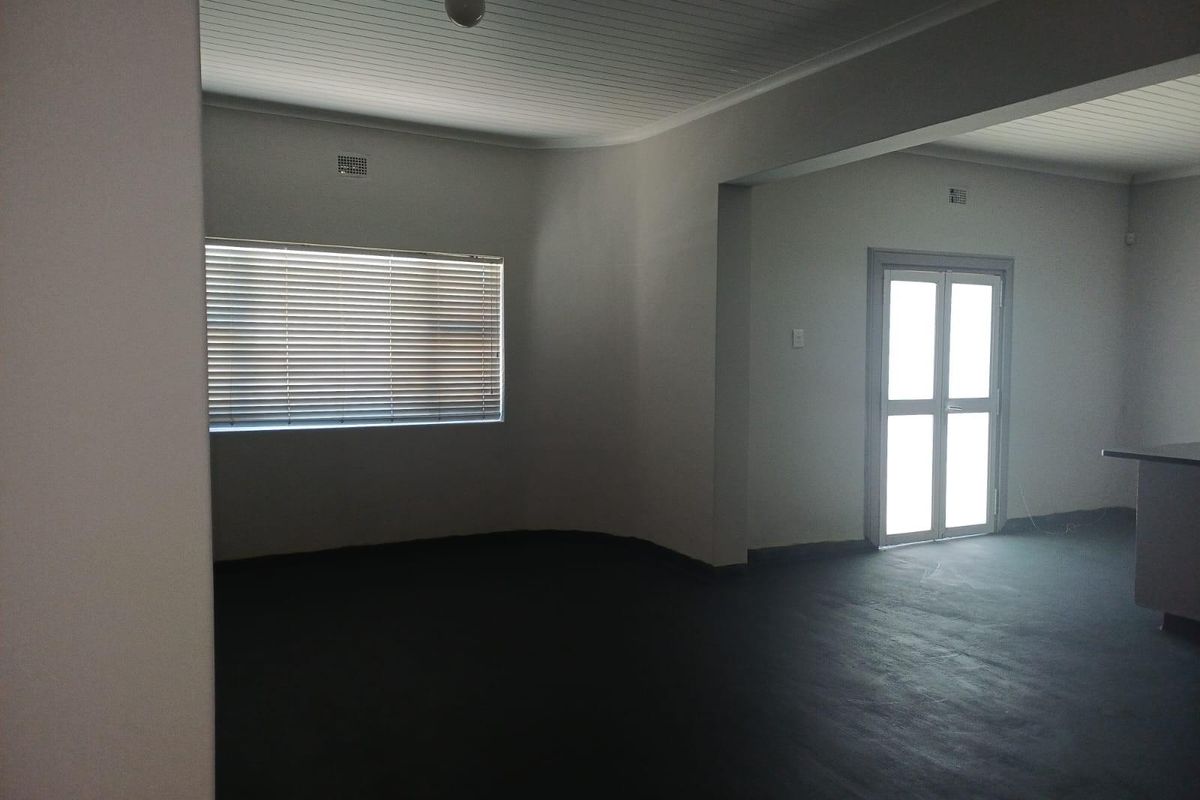 An open-plan living area featuring painted concrete flooring, a tongue-and-groove ceiling, and a glass-paneled door leading to the exterior.