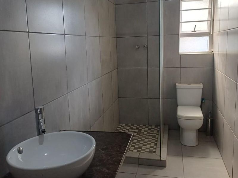 Modern bathroom featuring a walk-in shower with glass screen, a vessel sink on a stone vanity top, and a standard toilet.