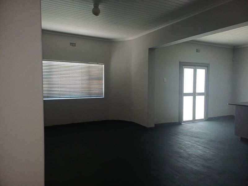 An open-plan living area featuring painted concrete flooring, a tongue-and-groove ceiling, and a glass-paneled door leading to the exterior.