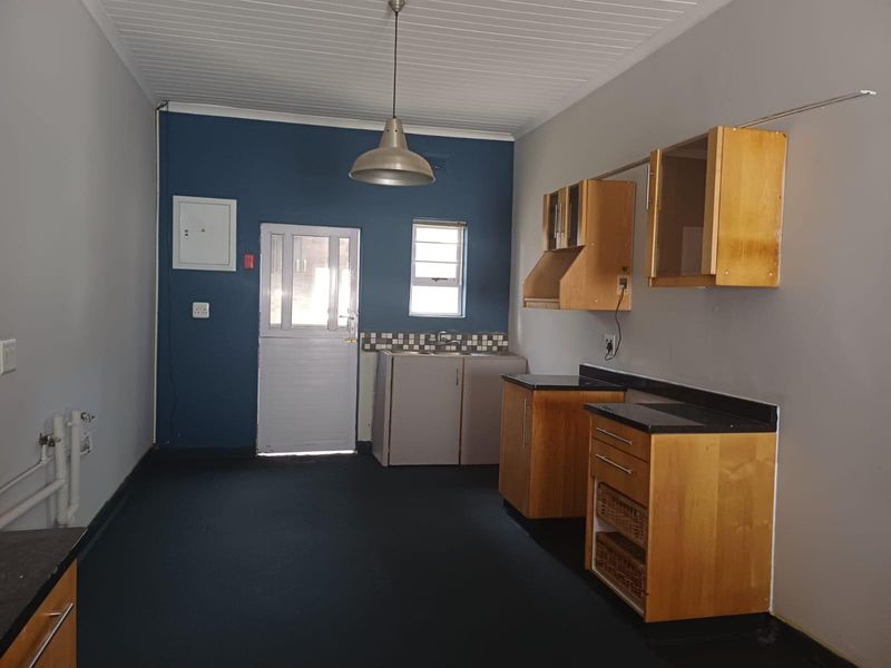 A functional kitchen area featuring wooden cabinetry, dark countertops, a single sink, and a stable-style exterior door with direct access.
