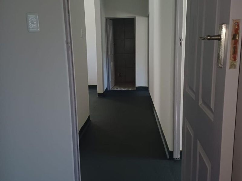 A functional interior hallway featuring dark flooring, white walls, and a tongue-and-groove ceiling, providing access to adjacent rooms.