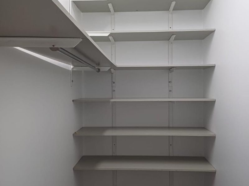 A functional walk-in storage closet or pantry featuring adjustable wall-mounted shelving units and a hanging rail.