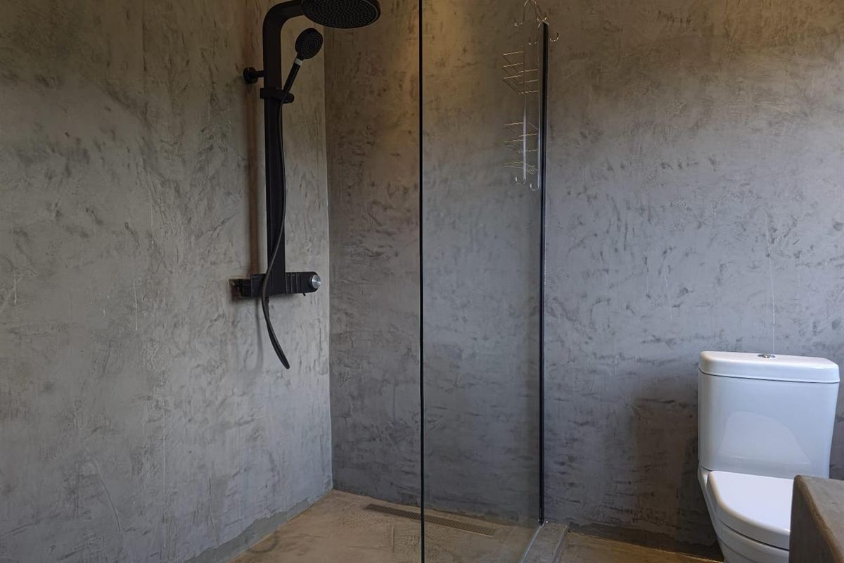 Modern bathroom featuring a walk-in shower with black fixtures, glass screen, and contemporary cement-look wall finishes.