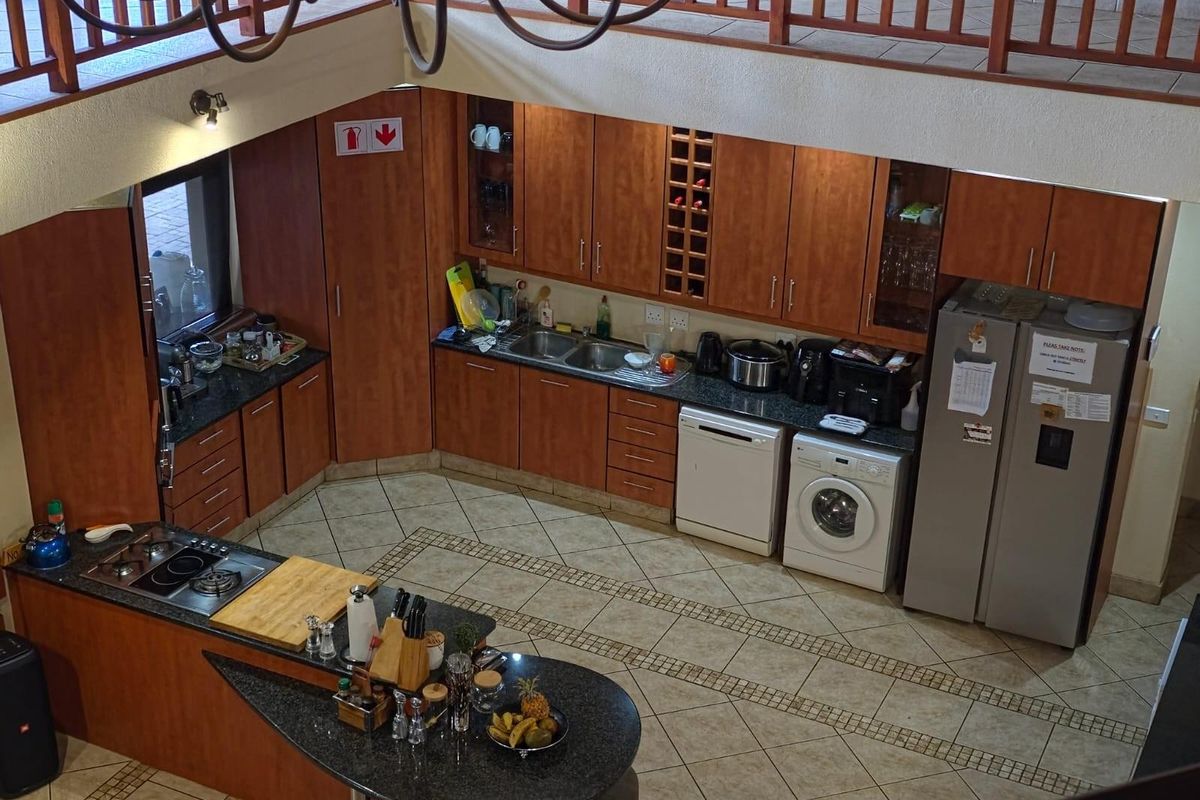 Spacious kitchen featuring wood-finish cabinetry, granite countertops, a central island with gas hob, and an open-plan layout overlooked by a mezzanine balcony.