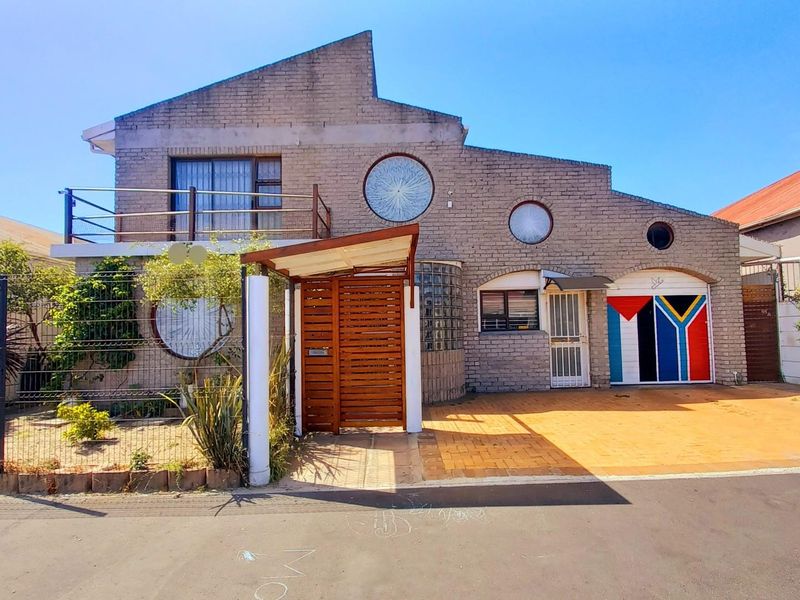 A unique two-story brick residence featuring distinctive circular windows, a private balcony, and a paved driveway with a secure gated entrance.