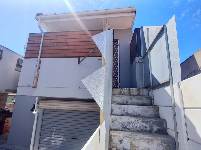 Exterior view of a multi-level property featuring a garage, external staircase with damaged balustrade, and timber cladding accents.