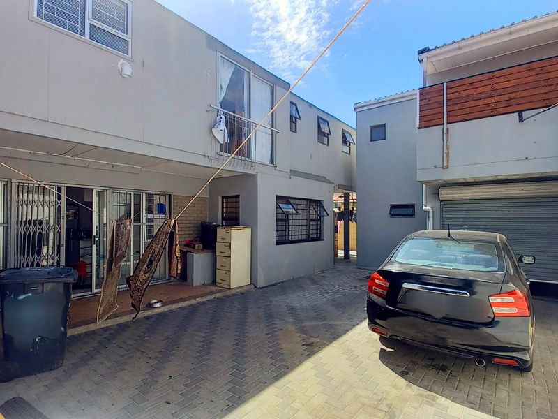 Rear exterior view of the property featuring a paved courtyard, garage access, and sliding door entry to the main living area.