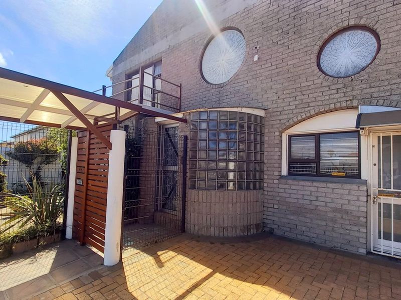 Front entrance area featuring a paved courtyard, covered walkway, glass block feature wall, and distinctive circular windows on the brick facade.