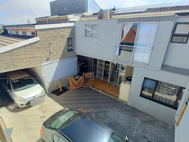 Rear exterior view of the property featuring a paved courtyard, covered parking area, and upper-level balcony access.