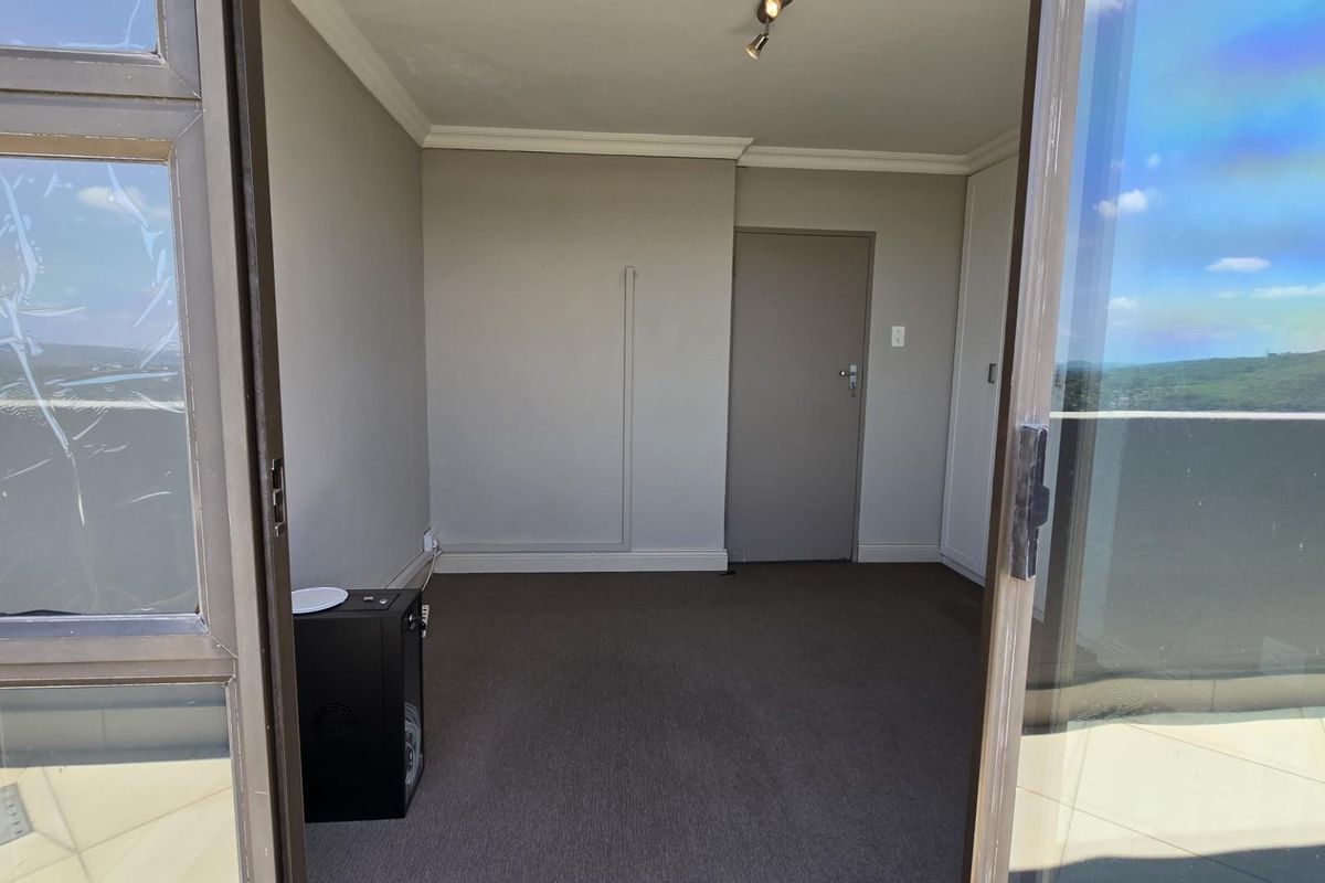 An empty bedroom featuring neutral walls, carpeted flooring, and direct access to a balcony through sliding glass doors.