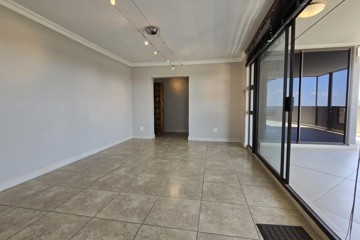 Spacious living area featuring large sliding glass doors that open onto a private balcony, finished with neutral floor tiles and crown molding.