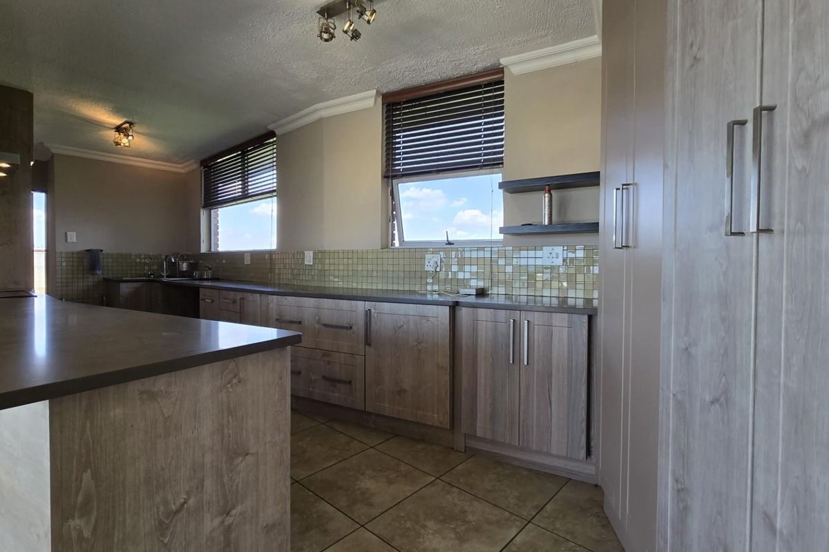A functional kitchen featuring wood-grain cabinetry, tiled backsplash, stone-look countertops, and tiled flooring with natural light from multiple windows.