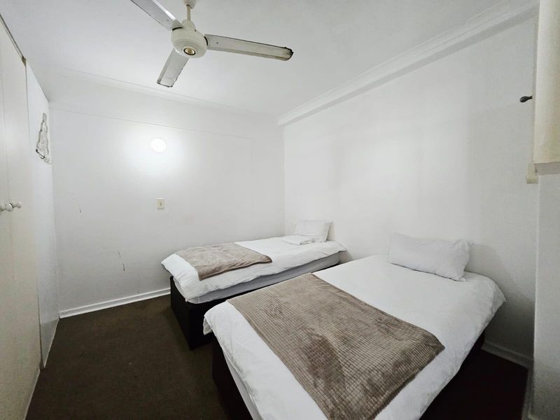 A compact bedroom featuring a ceiling fan and built-in storage, currently configured with twin beds.
