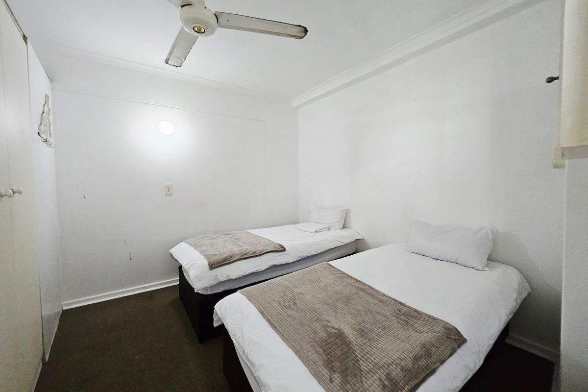 A compact bedroom featuring a ceiling fan and built-in storage, currently configured with twin beds.