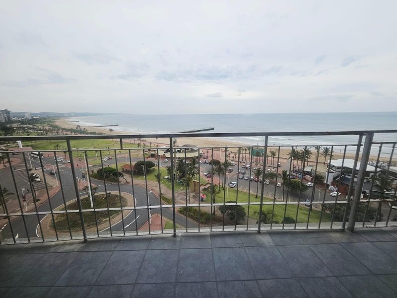A balcony offering expansive coastal and ocean views, featuring tiled flooring and a metal safety railing overlooking the beach and promenade.