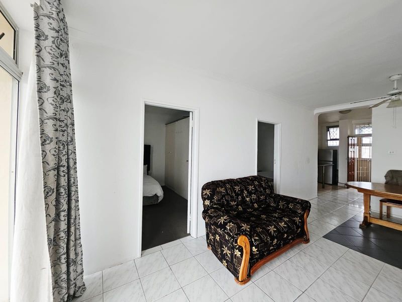 Open plan living area featuring tiled flooring, leading into a kitchen and adjacent bedroom space.