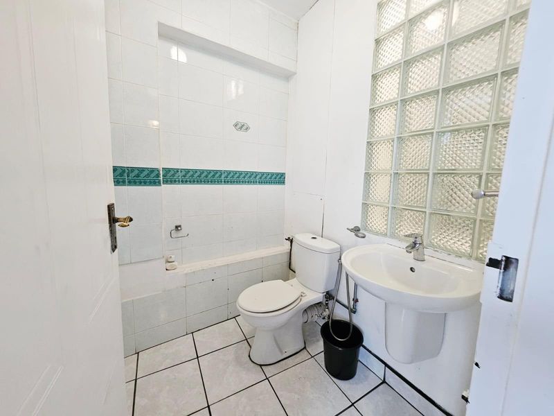 A functional bathroom featuring a pedestal sink, toilet, and tiled walls with a glass block feature window for natural light.