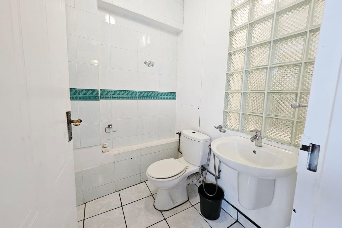 A functional bathroom featuring a pedestal sink, toilet, and tiled walls with a glass block feature window for natural light.