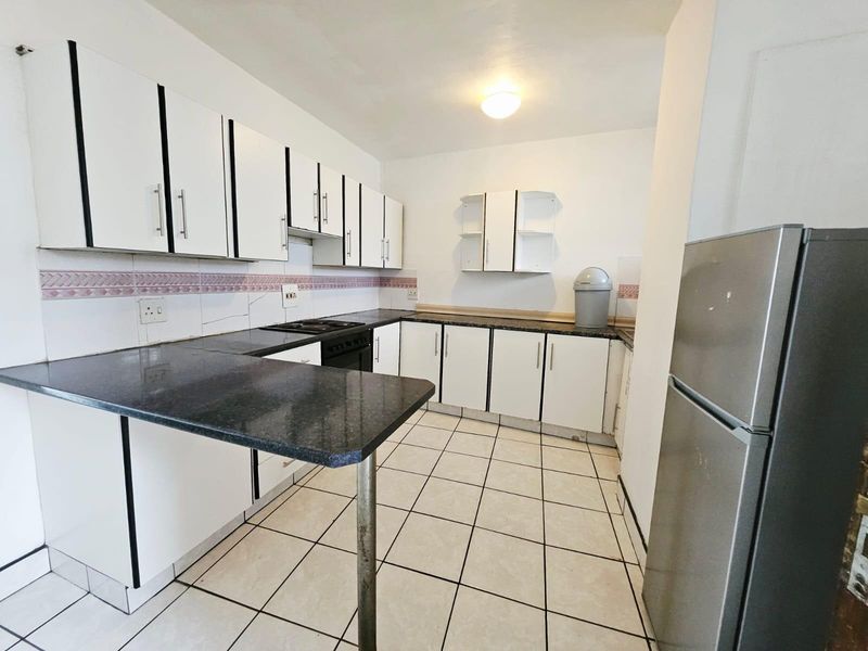A functional kitchen featuring white cabinetry, dark countertops, a built-in hob, and tiled flooring, offering a practical layout for daily meal preparation.