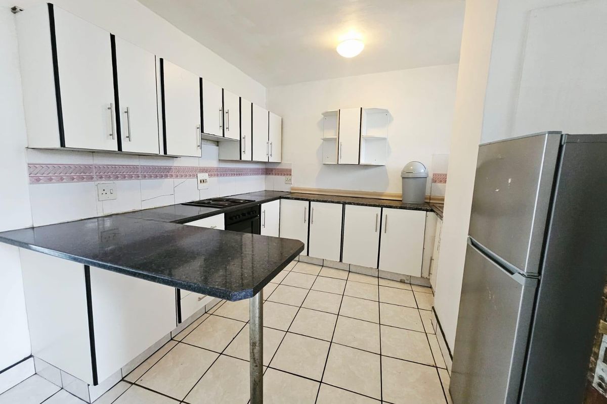 A functional kitchen featuring white cabinetry, dark countertops, a built-in hob, and tiled flooring, offering a practical layout for daily meal preparation.