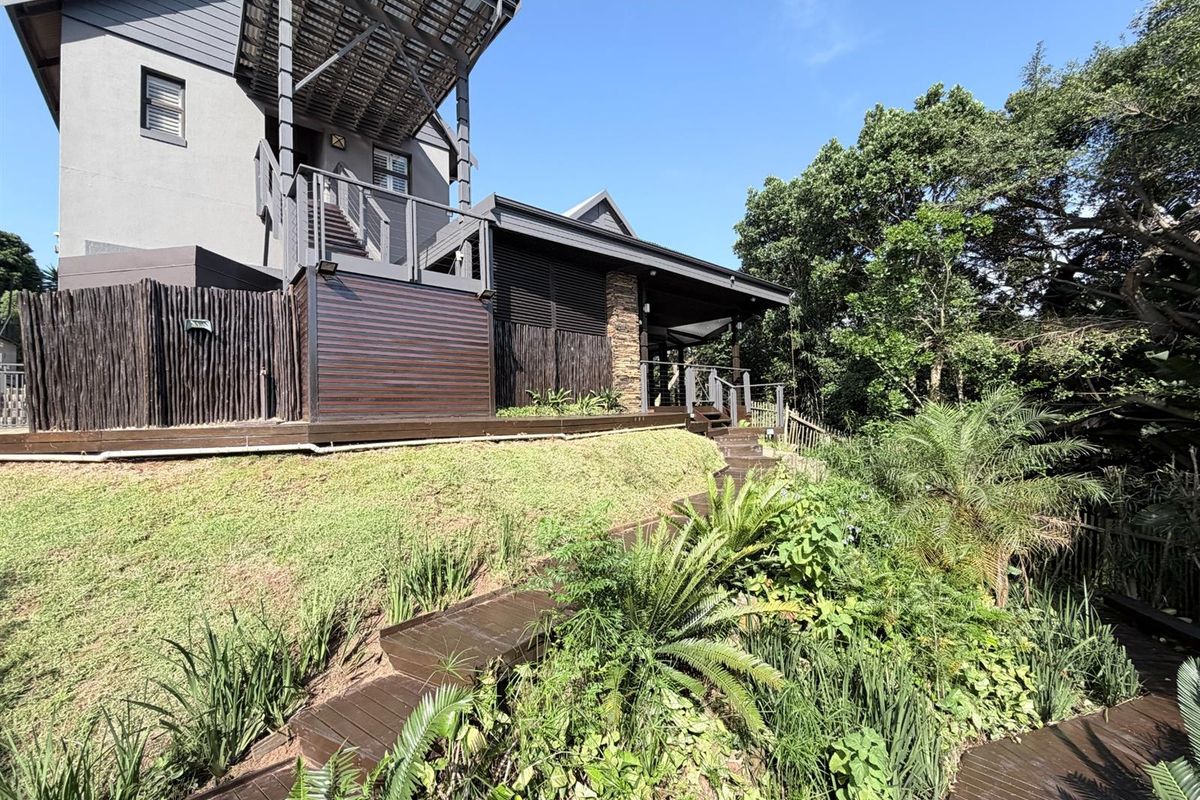 A view of the rear exterior of the house, featuring a multi-level timber deck, staircase, and landscaped garden area.