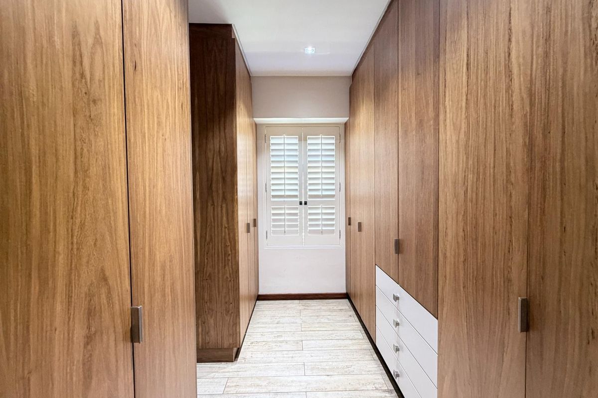 A well-appointed walk-in closet featuring extensive floor-to-ceiling wooden cabinetry, integrated drawers, and plantation shutters on the window.