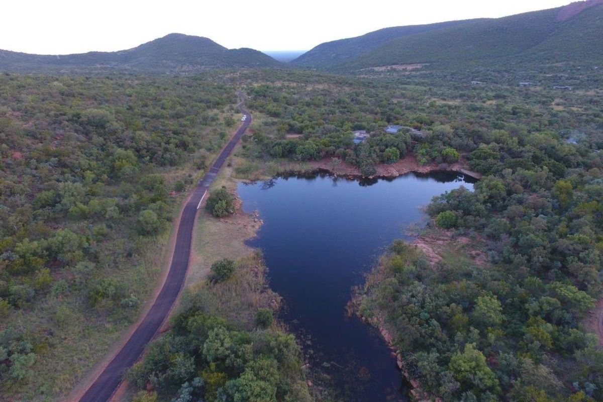 An aerial view of the vacant residential land featuring natural vegetation, a scenic dam, and access to a paved road within a mountainous landscape.