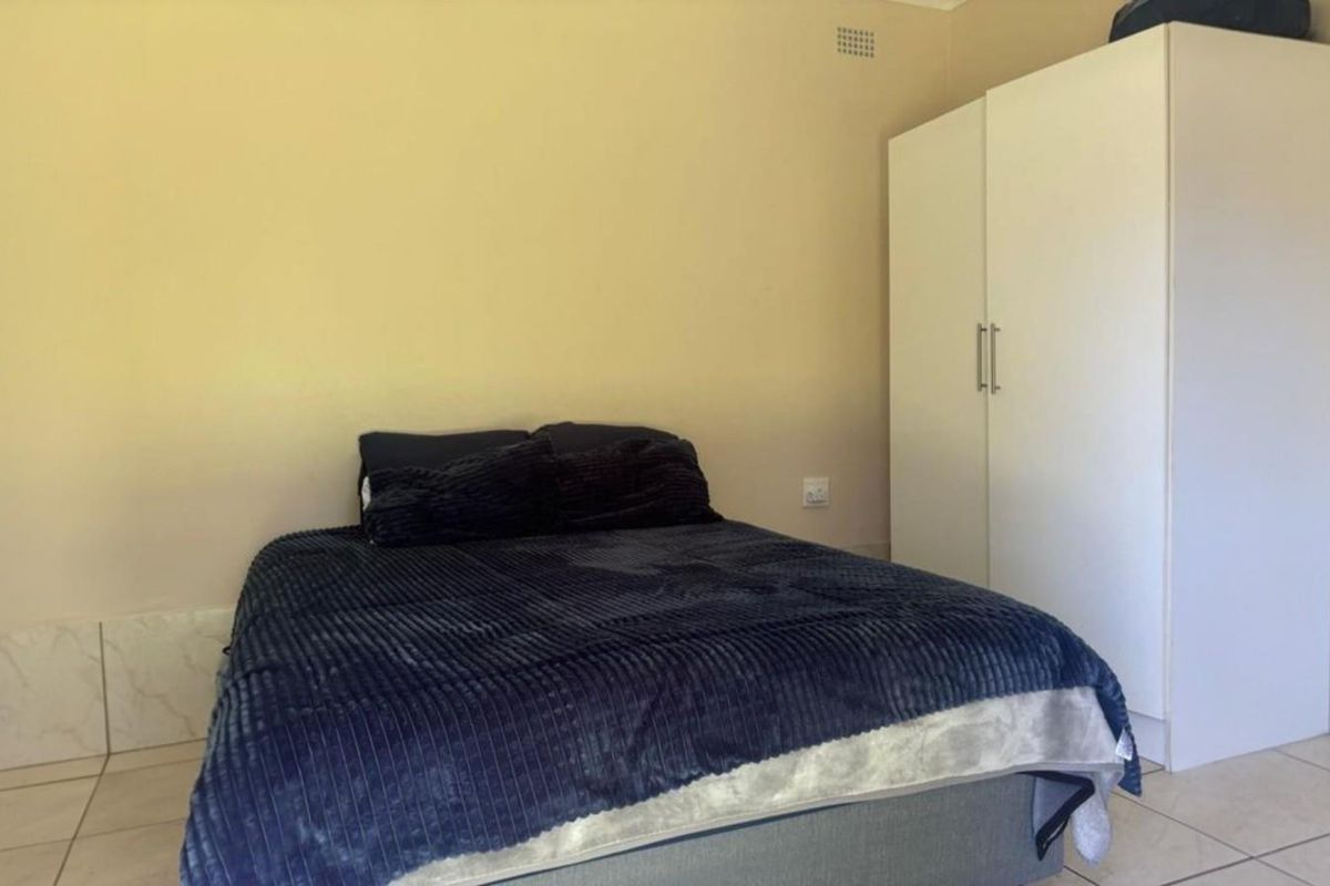 A simple bedroom featuring tiled flooring and a built-in wardrobe, offering a functional and neutral space.