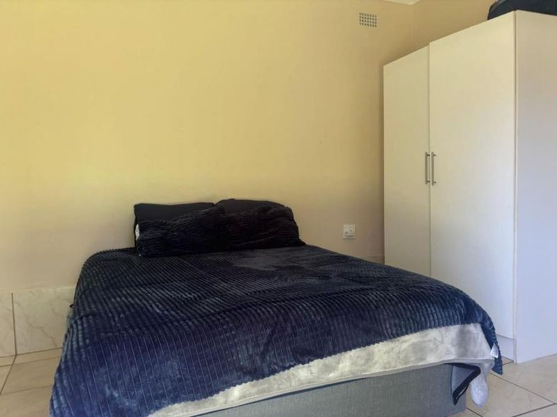 A simple bedroom featuring tiled flooring and a built-in wardrobe, offering a functional and neutral space.